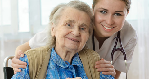 Seated older woman with a younger carer crouched by her side with both hands on her shoulders